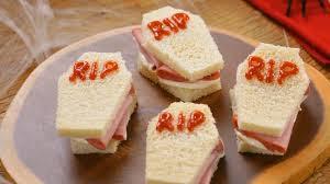 Corte as fatias de pão de forma em formato de mini caixões.Adiciona o requeijão cremoso e a Mortadela Ouro.Feche o sanduíche e decore com ketchup ou geleia de pimenta.