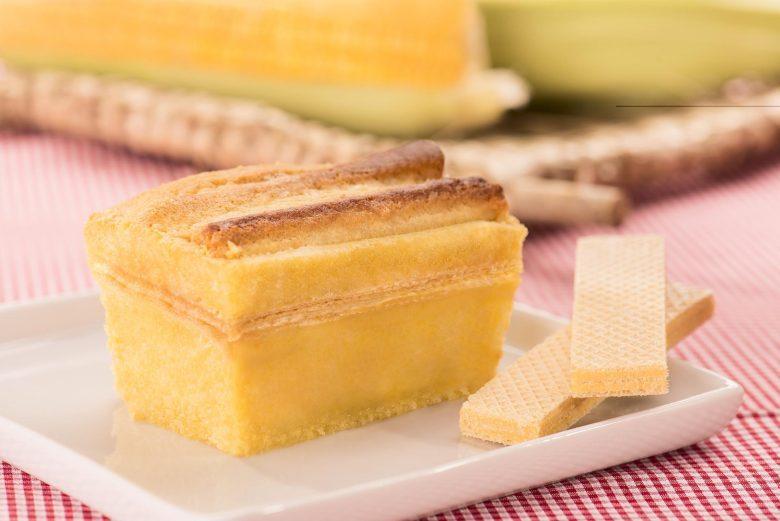 Derreta a margarina com o chocolate branco picado em banho-maria.Bata os ovos com o milho no liquidificador, depois misture em um recipiente com o trigo, a mistura do chocolate com a manteiga, e a essência de baunilha.Coloque em uma forma de bolo inglês untada e enfarinhada, uma camada da massa, o biscoito wafer e cubra com o restante da massa.Leve ao forno de 30 a 40 minutos a 180c.